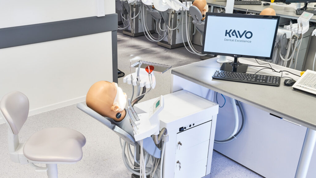 A dental simulation setup featuring a realistic dental mannequin, dental instruments, and a computer screen displaying "KAVO Dental Excellence."