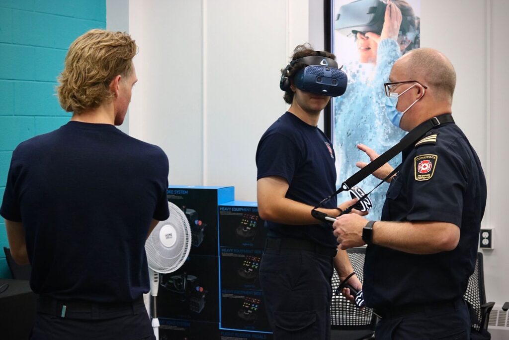 Firefighting trainees use a VR headset during a training session with an instructor from Conestoga Fire Services, featuring XpertVR technology.