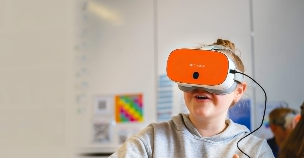 A student wearing an orange ClassVR headset from Avantis Education engages with an immersive virtual reality learning experience in a classroom.