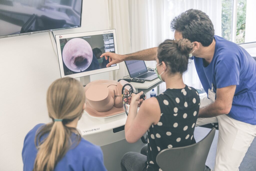 Medical trainees using an advanced endoscopy simulator with a monitor displaying the internal view of a virtual organ, guided by an instructor.