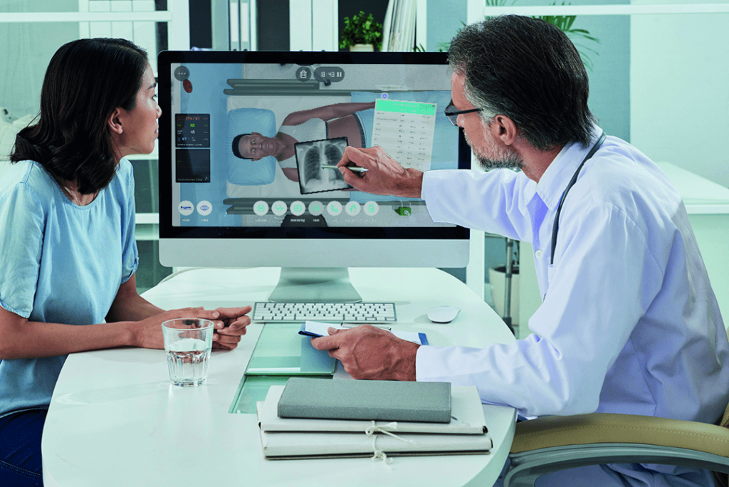 A doctor and a trainee discussing a virtual patient simulation displayed on a computer screen, including diagnostic tools and patient data.