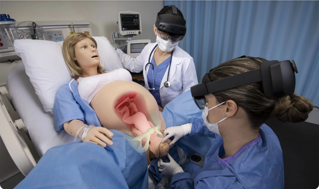 Two healthcare trainees wearing augmented reality headsets practice an obstetric emergency simulation on a high-fidelity mannequin showing a realistic birthing process.